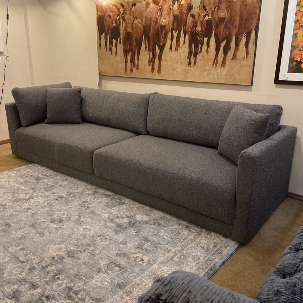 Gray sectional sofa in a room with a large painting of cows on the wall.