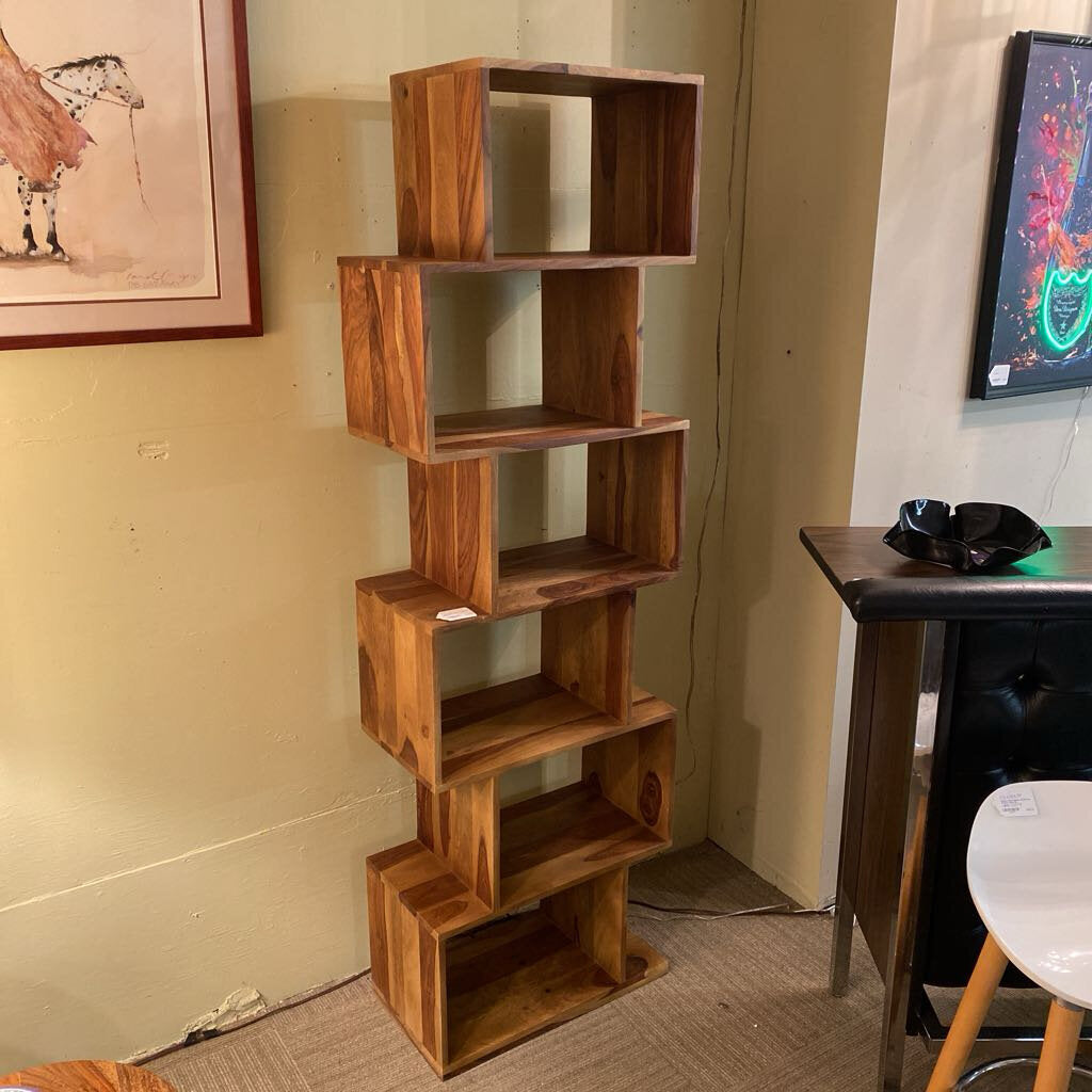 Wooden geometric shelf in a room with a chair and colorful painting on the wall.