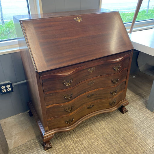 Wooden desk with curved design in a room with windows and carpeted floor.