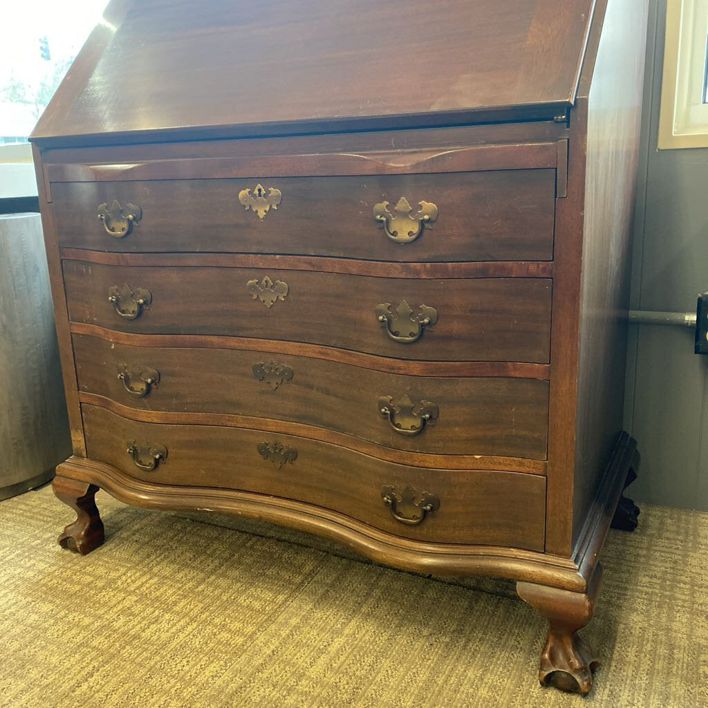Wooden dresser with curved design and multiple drawers on a carpeted floor.