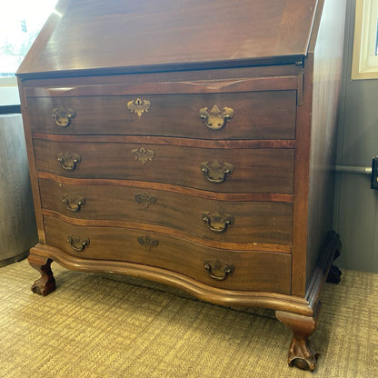 Wooden dresser with curved design and multiple drawers on a carpeted floor.
