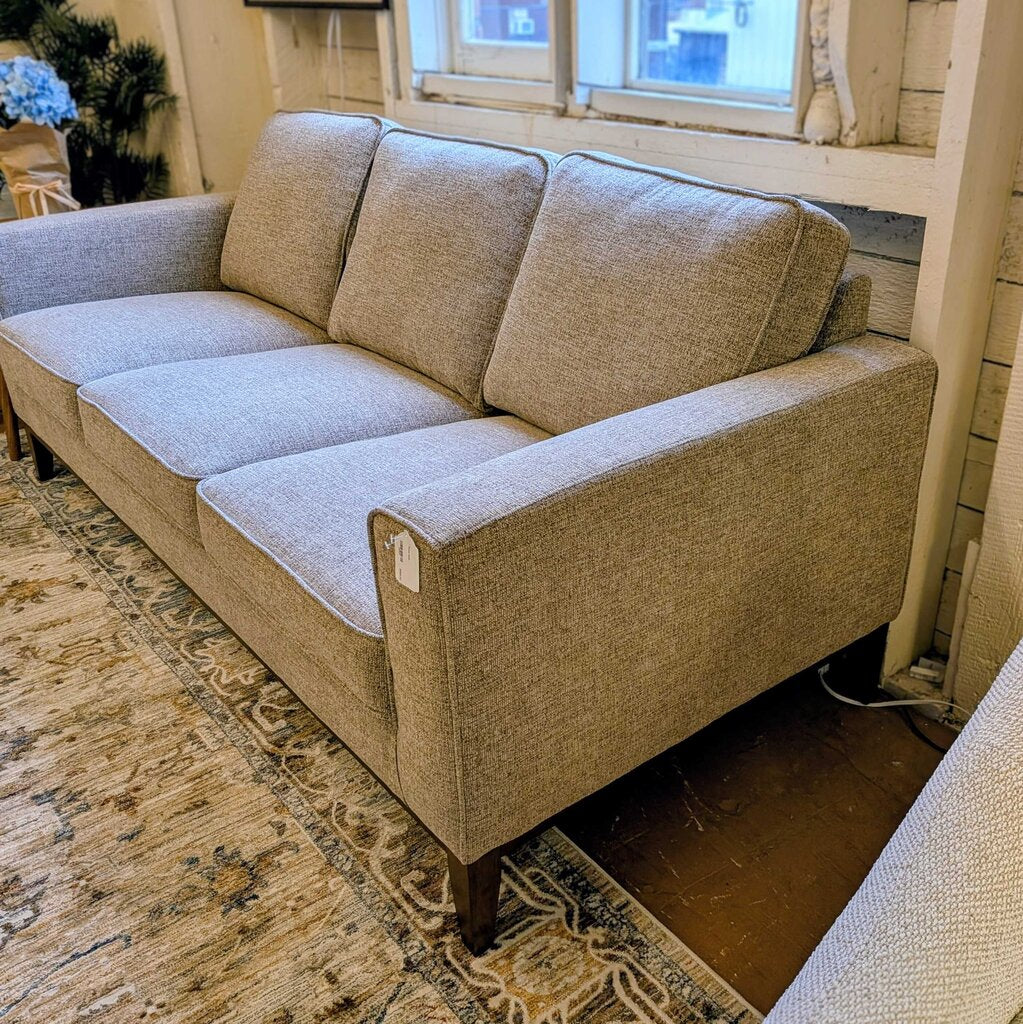 Beige sectional sofa in a living room setting with a rug and window in the background.