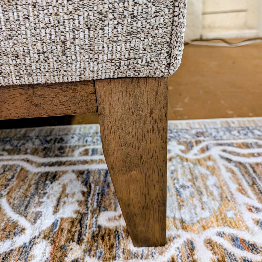 Close-up of a textured chair seat and wooden leg on a patterned rug.