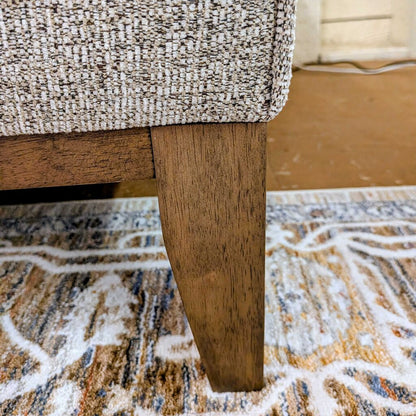 Close-up of a textured chair seat and wooden leg on a patterned rug.