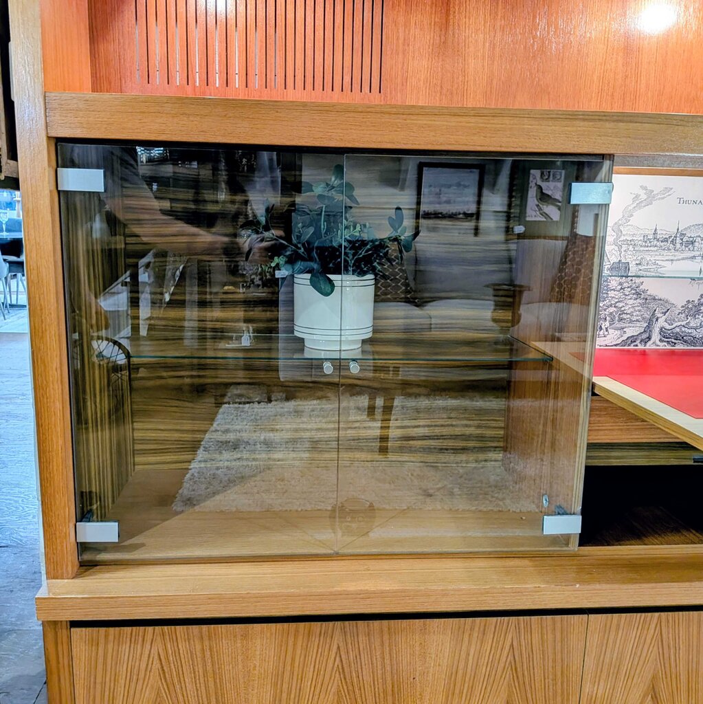 Wooden display case with glass front, interior showing a plant and furniture.