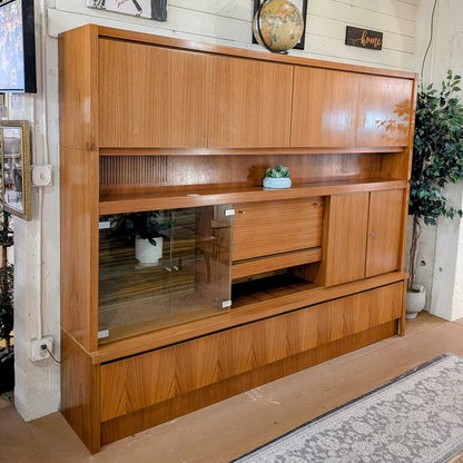 Wooden entertainment console with glass shelves in a living room setting.