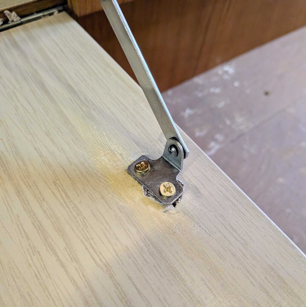 Metal bracket attached to a wooden surface with screws.