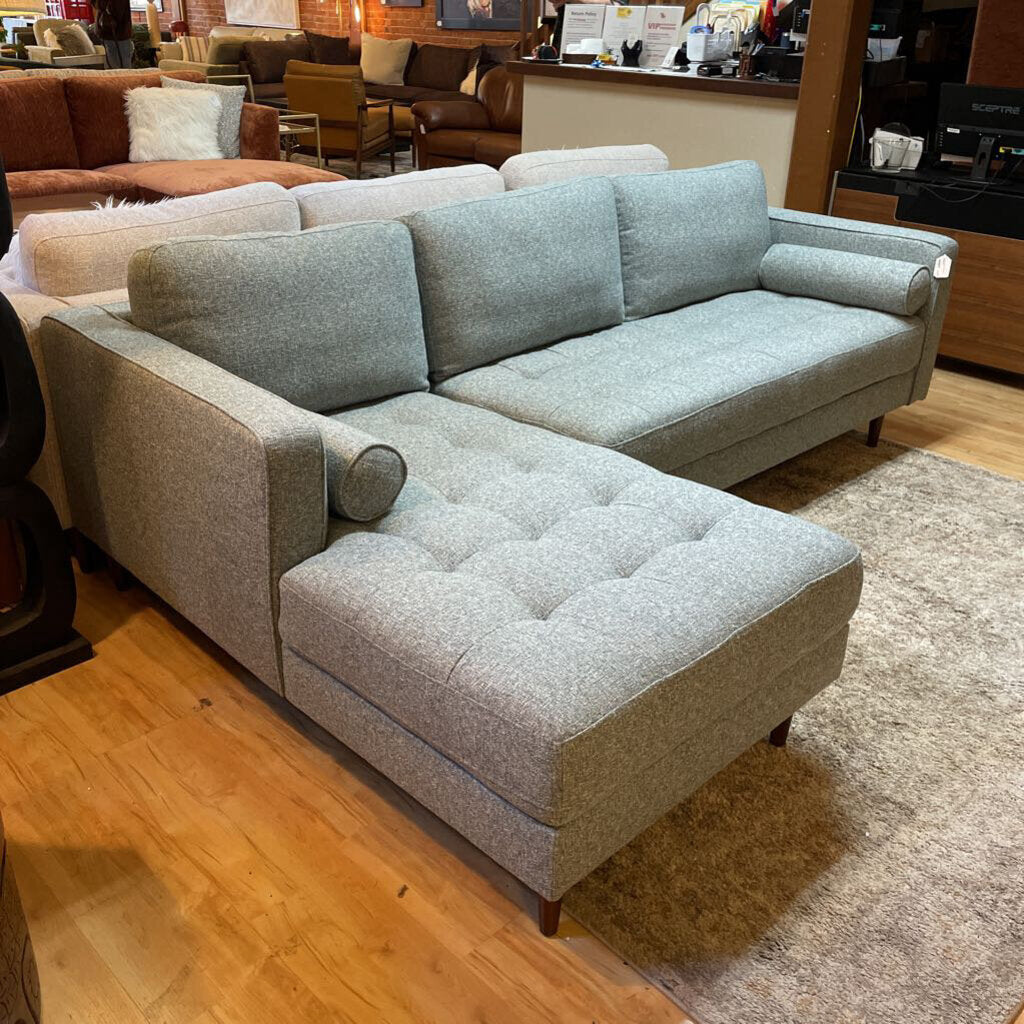 A light grey textured fabric sectional sofa featuring a left-arm-facing chaise with button-tufted seat cushions, two matching bolster pillows, and tapered wooden legs.