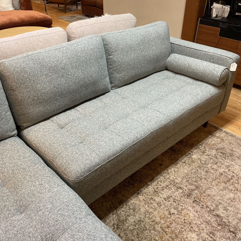 A light grey textured fabric sectional sofa featuring a left-arm-facing chaise with button-tufted seat cushions, two matching bolster pillows, and tapered wooden legs.