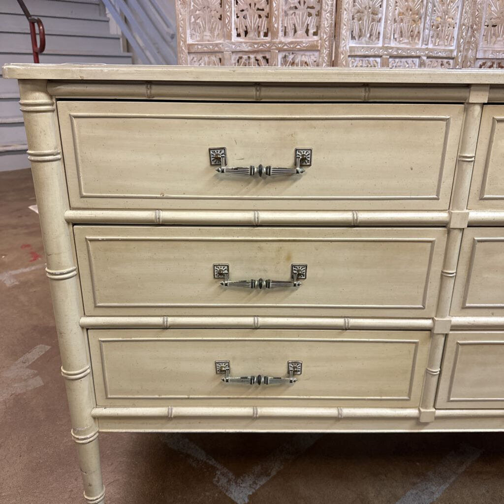 Beige dresser with three drawers and decorative handles on a concrete floor.