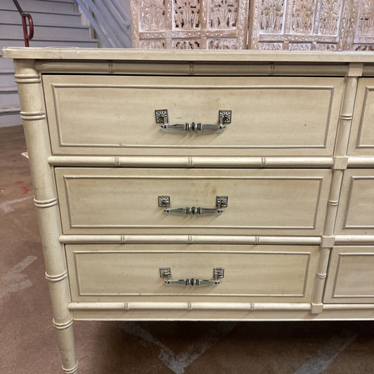 Beige dresser with three drawers and decorative handles on a concrete floor.