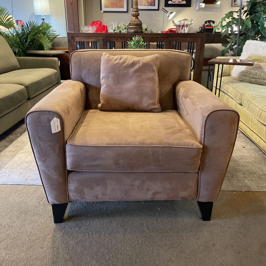 Brown armchair with a pillow in a room with furniture and decor.