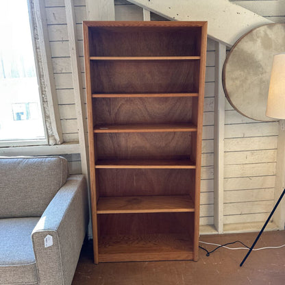 Wooden bookshelf next to a gray sofa in a room with wooden walls.