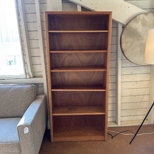 Wooden bookshelf next to a gray sofa in a room with wooden walls.