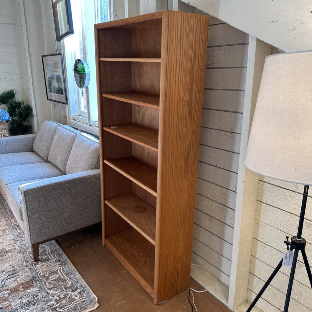 Wooden bookshelf next to a gray sofa in a living room setting.