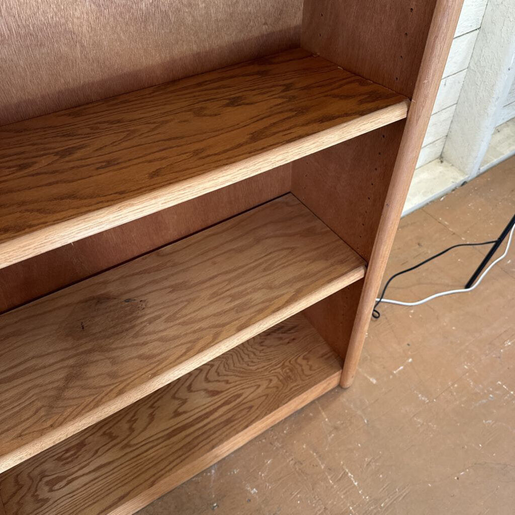 Wooden bookshelf with three shelves on a tiled floor.