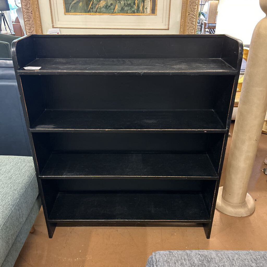 Black metal bookshelf on a wooden floor with a blurred background