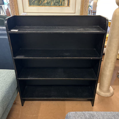 Black metal bookshelf on a wooden floor with a blurred background