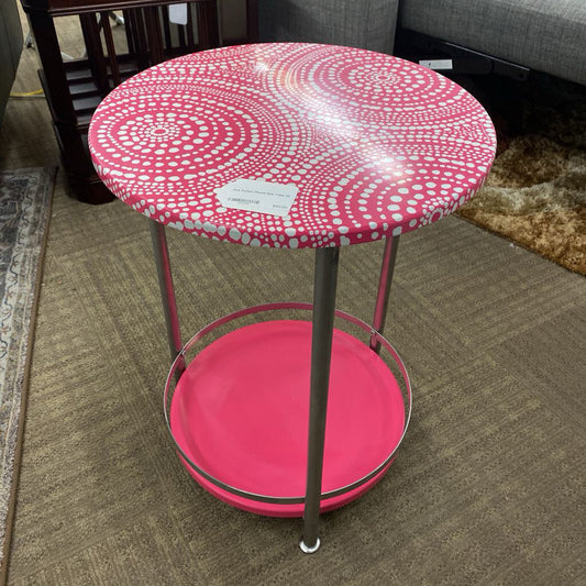 Small round table with pink and white patterned top and pink base on a carpeted floor.
