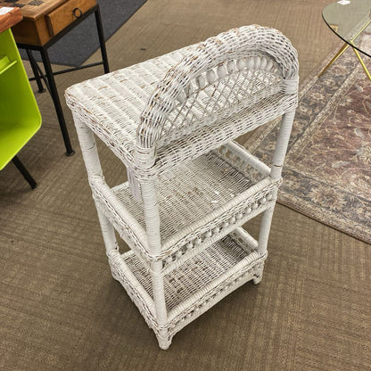 White wicker side table in a room with a green chair and wooden desk.