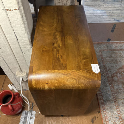 Wooden dresser with a red pitcher on the floor next to it, in a room setting.