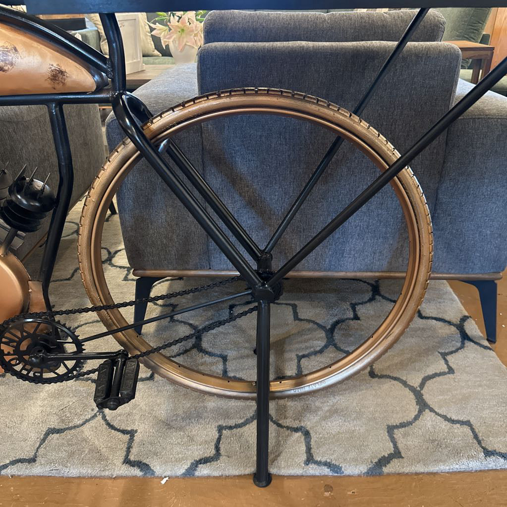 Close-up of a bicycle wheel and frame on a patterned rug with a couch in the background