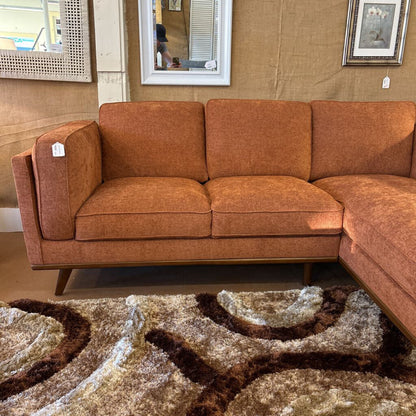 Brown sectional sofa in a room with a patterned rug and mirrors on the wall.