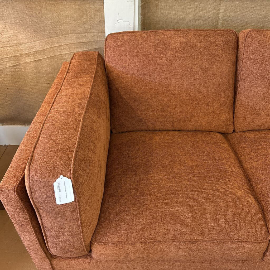 Brown sofa with a visible tag in a room with beige walls.