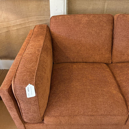 Brown sofa with a visible tag in a room with beige walls.
