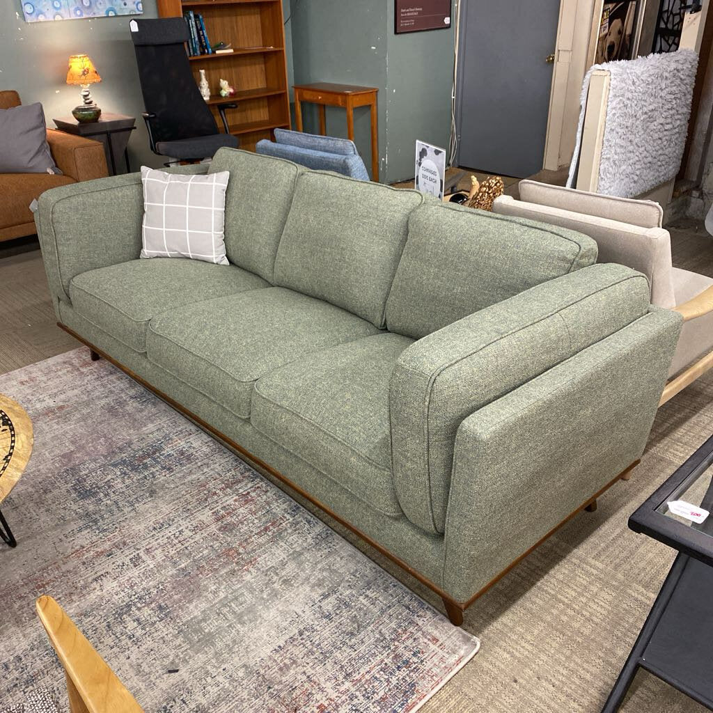 Green sofa with a pillow in a room with other furniture and decor.