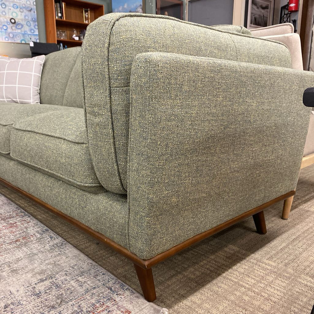 Green upholstered sofa with wooden legs in a room setting