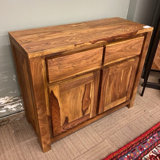 Wooden sideboard with drawers and doors against a plain wall.