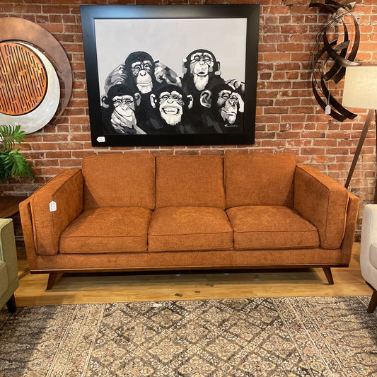 Brown sofa in a room with a brick wall and framed artwork of monkeys.