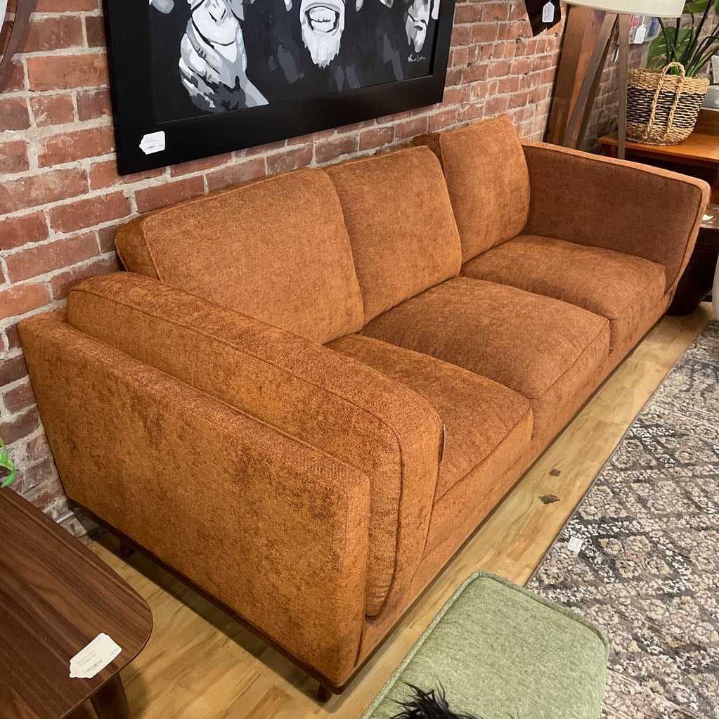 Brown sofa in a room with a brick wall and a TV.