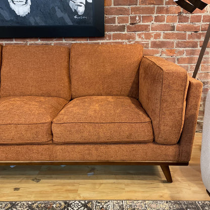Brown sofa in a room with a brick wall and a painting.