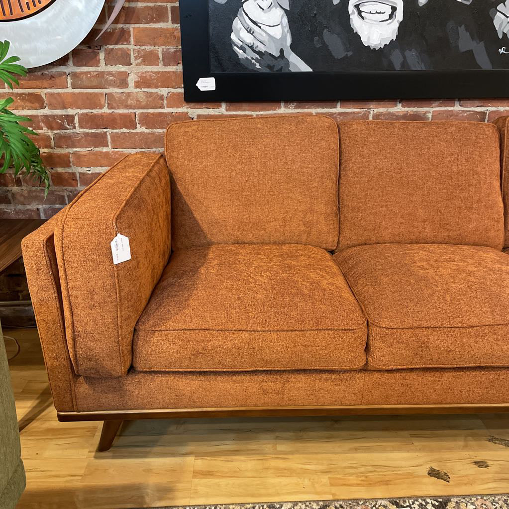 Brown sofa with a price tag in front of a brick wall and artwork.