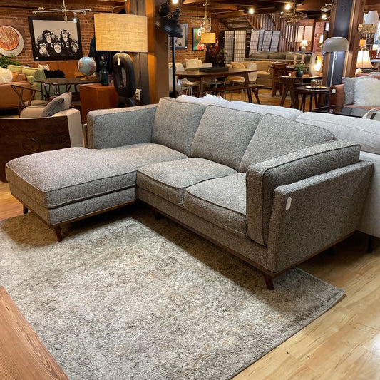 Gray sectional sofa in a room with wooden floors and furniture.