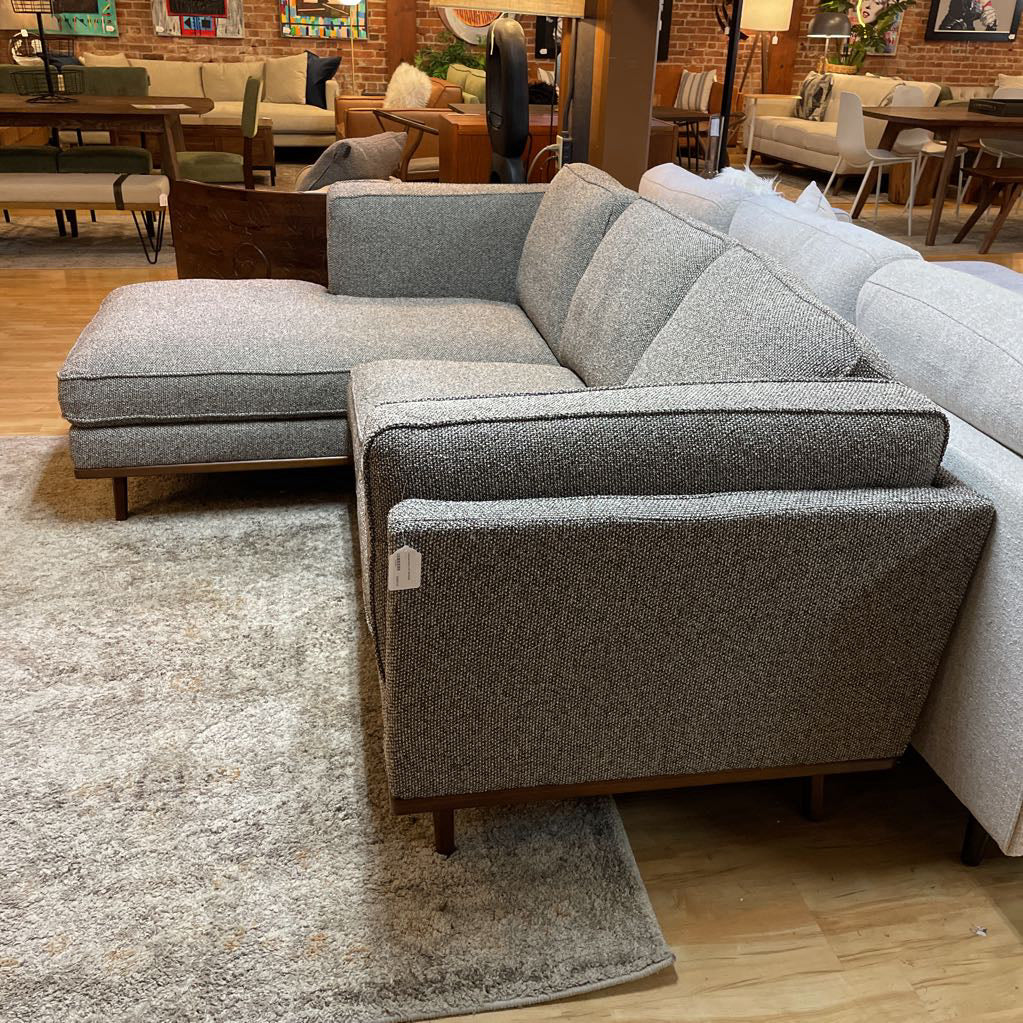 Gray sectional sofa in a showroom setting with other furniture in the background.