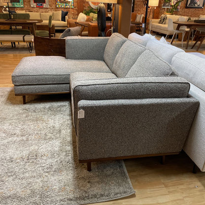 Gray sectional sofa in a showroom setting with other furniture in the background.