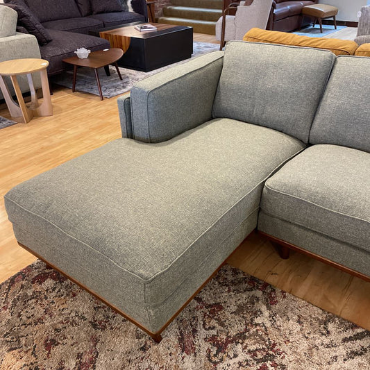 Gray sectional sofa in a living room setting with wooden floors and furniture.