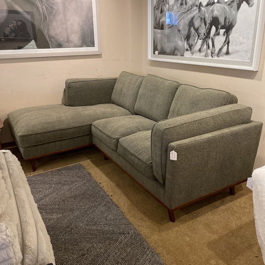 Green sectional sofa in a room with horse pictures on the wall.