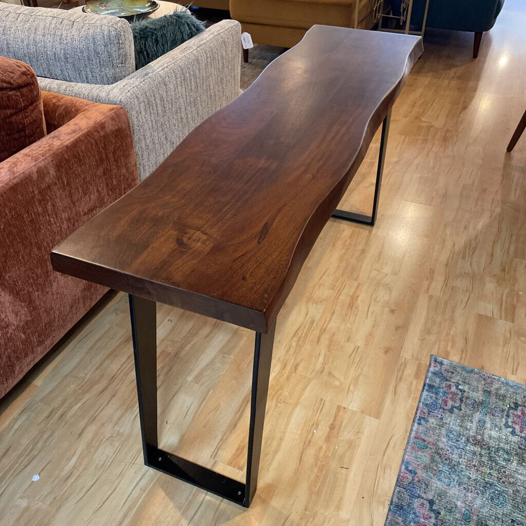 Wooden dining table with black metal legs in a room with furniture and decor.