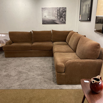 Brown sectional sofa in a living room setting with a rug and wall art.