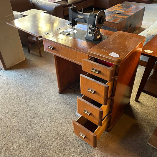 Vintage wooden sewing machine on a desk with drawers in a room setting.