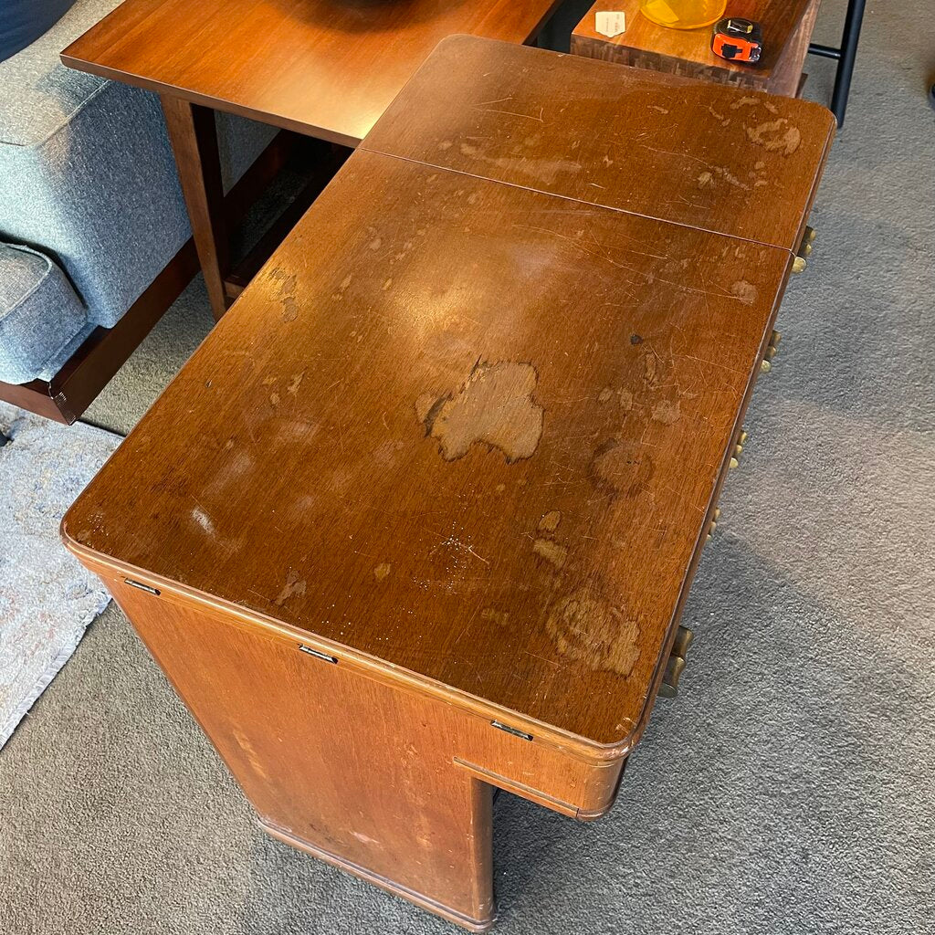 Old wooden desk with visible wear and tear on a carpeted floor.