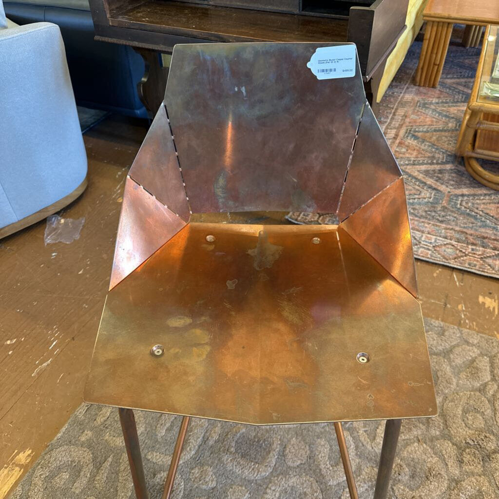 Bronze or copper metal chair with a textured surface on a patterned rug.