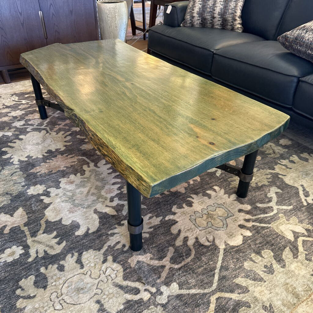 Wooden coffee table with black legs on a patterned rug in a living room setting.