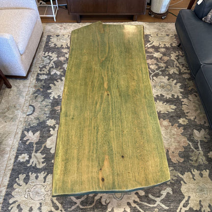 Large green wooden board on a patterned rug in a living room setting