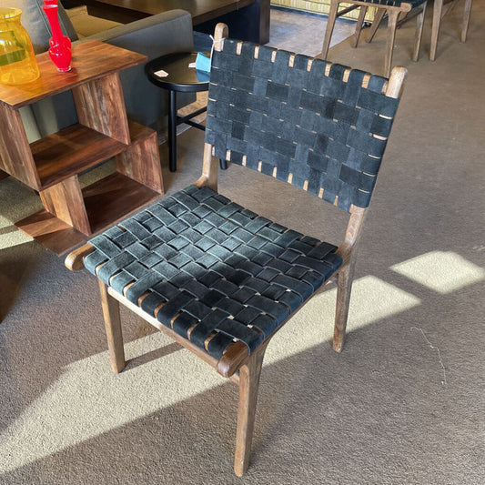 Chair with woven blue seat and backrest in a room with wooden furniture and a rug.