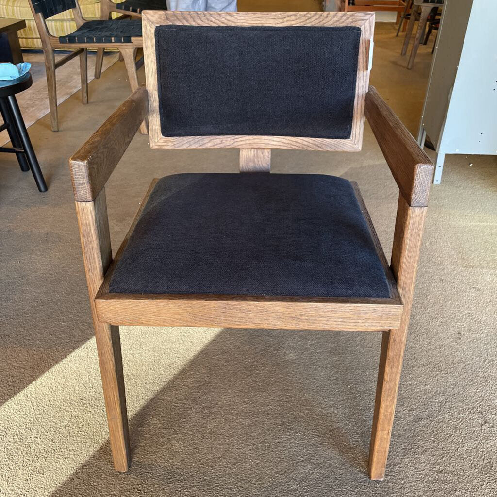 Wooden chair with black cushioned seat and backrest on a carpeted floor.